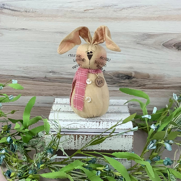 Beige bunny with pink plaid scarf standing on a piece of wood