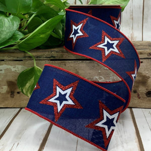 Roll of navy ribbon with red and white glitter stars posed with green leaves